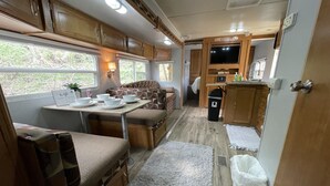 Interior compacto de autocaravana con kitchenette, zona de estar y una televisión pequeña.