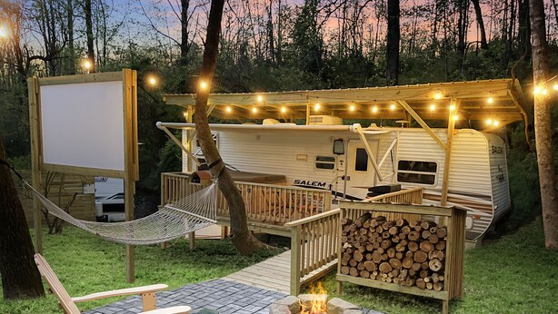 Un camping con una hamaca, un hoyo para el fuego, una terraza y una caravana.