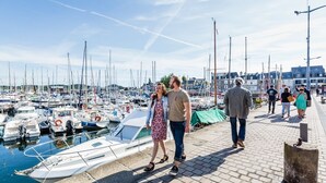 Un port de plaisance avec des bateaux amarrés, un couple qui se promène et une promenade pavée.
