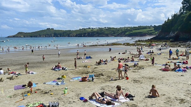 Une plage bondée où les gens se prélassent au soleil et se baignent.