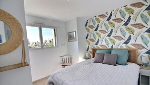 Une chambre à coucher avec un lit, une chaise, une fenêtre et un mur orné d’un motif de feuilles.