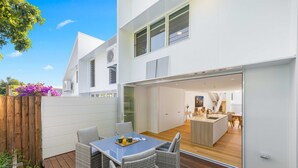 Une maison moderne dotée d’un patio aménagé avec des meubles en osier et une table en verre.