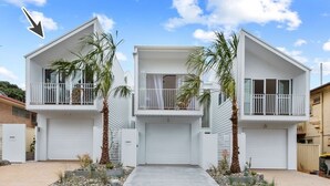 Une maison moderne à deux étages, dotée d’un garage, d’un chemin d’accès à l’entrée et de deux palmiers.