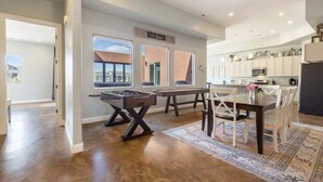 A spacious living area with a foosball table, a dining table with chairs, and a kitchen area with cabinets and appliances.