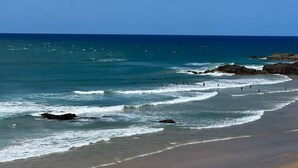 Une plage avec une eau d’un bleu limpide, des affleurements rocheux et une rive sablonneuse.