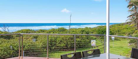 A deck with a table and chairs overlooking a coastal view.