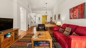 A living room with a television, a red sofa, a wooden coffee table, and a dining area in the background.