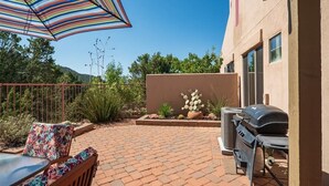 A patio with a grill, outdoor furniture, and a striped umbrella.