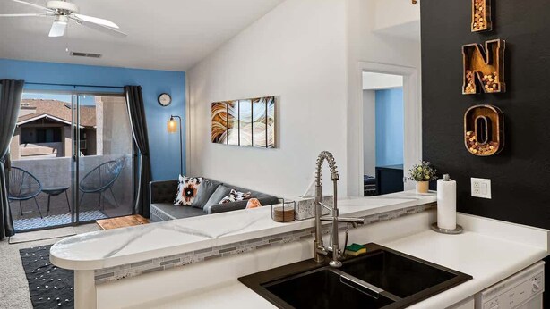 Une cuisine moderne avec un évier noir, des plans de travail blancs et un ventilateur de plafond.
