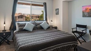 Une chambre à coucher avec un lit, un bureau, une chaise, une fenêtre avec des rideaux et un tableau au mur.