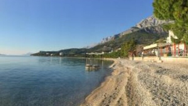 A coastal scene with a pebble beach, a clear sky, and a mountain in the background. - Villa Radalj (Makarska)