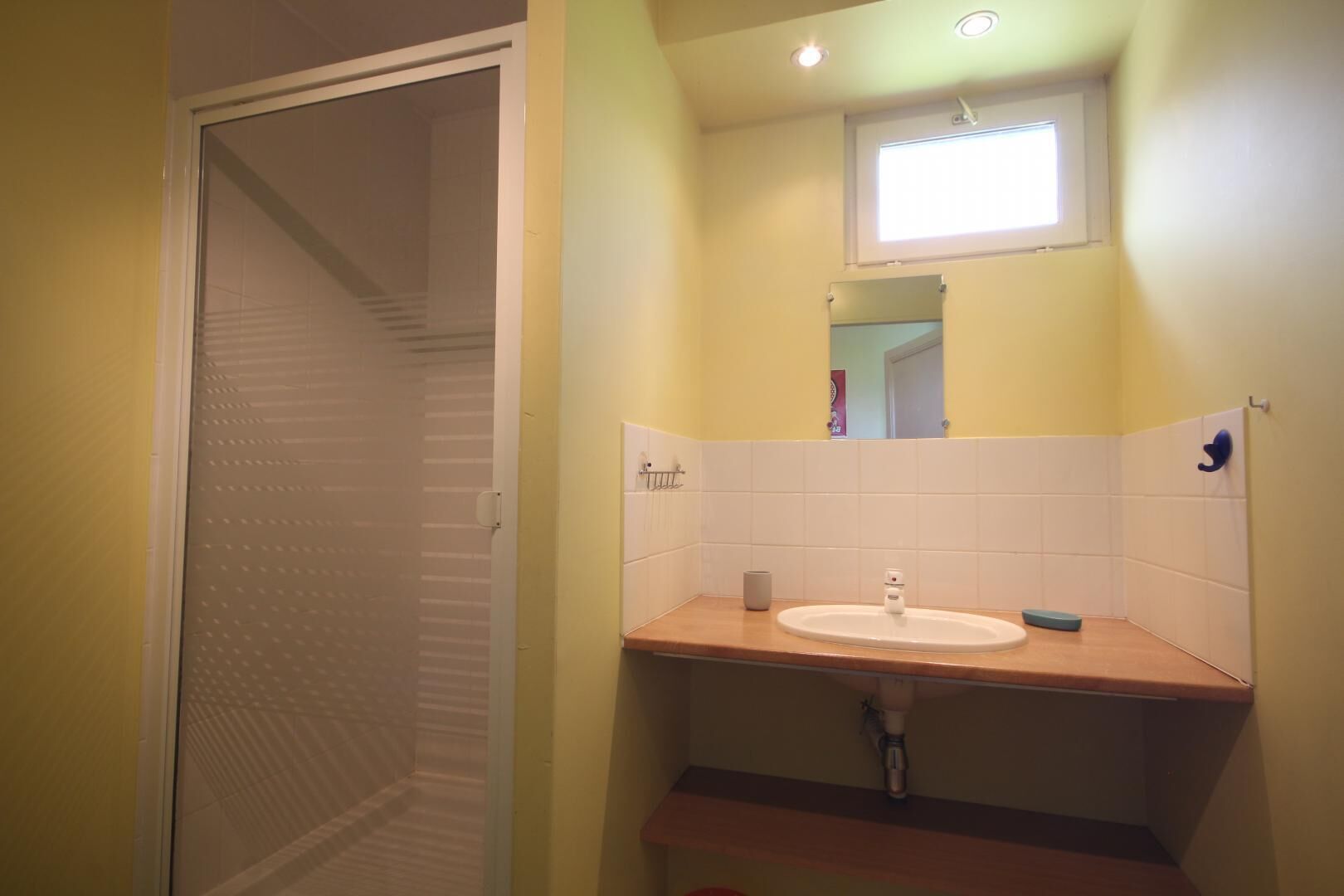 A bathroom with a wooden countertop, a white sink, a small mirror, and a window above the mirror.