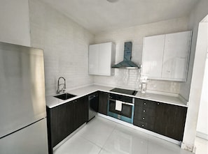 Una cocina moderna con armarios blancos, un refrigerador de acero inoxidable, lavavajillas y horno empotrado.