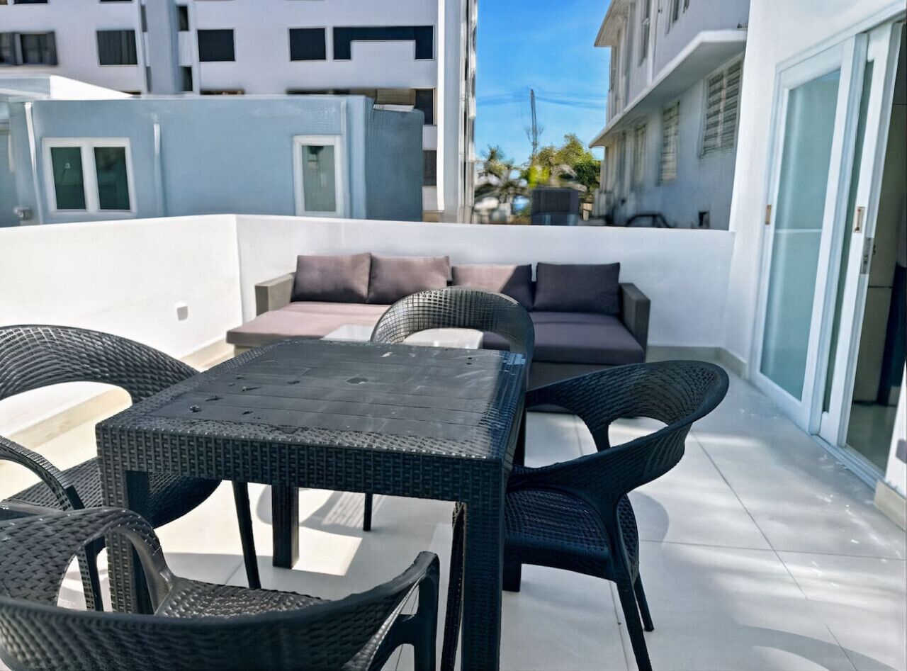 Terraço no telhado com mesa e cadeiras, um sofá e vista para edifícios vizinhos.