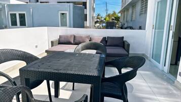 Terraço no telhado com mesa e cadeiras, um sofá e vista para edifícios vizinhos.