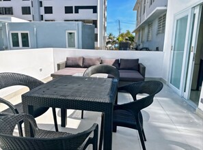 Una terraza en la azotea con mesa y sillas, un sofá y vistas a edificios cercanos.