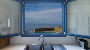 Cozinha com vista para o mar pela janela, pia dupla e tomada.