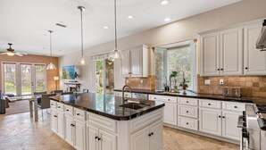 A spacious kitchen with white cabinetry, a large island with a sink, and pendant lighting. - Casa Azul (Poway)