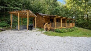 A rustic cabin with a covered porch and a small deck, surrounded by dense forest. - Modern Cabin w/ Trail to Waterfall/Cave/Cliff (TF) (Rockbridge)