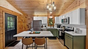 A modern kitchen with wooden walls, a central island, and a black door. - Modern Cabin w/ Trail to Waterfall/Cave/Cliff (TF) (Rockbridge)