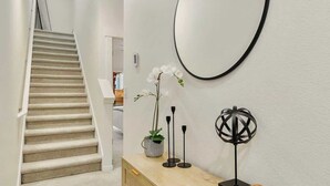 A hallway with a staircase, a wooden console table with a mirror, and a vase with white flowers.