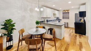 A modern kitchen with white cabinets, a marble island, and a dining area with wooden chairs.