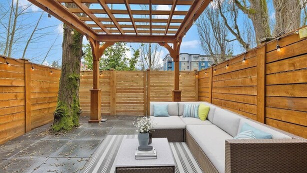 A covered patio area with a wooden pergola, a cushioned seating area, and a small table with a vase and book.