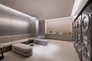 A modern laundry room with a sofa, ottoman, and a washing machine area.