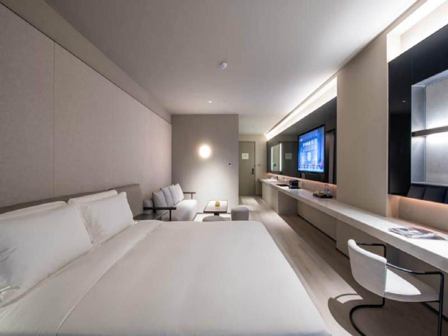 Quarto de hotel moderno com uma cama grande, uma escrivaninha com cadeira, televisão e um pequeno espaço de estar.