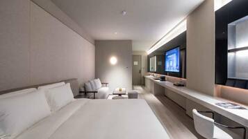 Quarto de hotel moderno com uma cama grande, uma escrivaninha com cadeira, televisão e um pequeno espaço de estar.