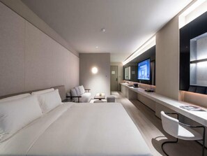 Een moderne hotelkamer met een groot bed, een bureau met stoel, een televisie en een zithoekje.