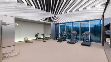 Academia moderna com equipamentos de ginástica, um espelho grande e vista da cidade através de amplas janelas.