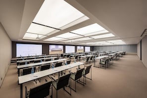 A conference room with multiple tables and chairs, large windows, and a projector screen.