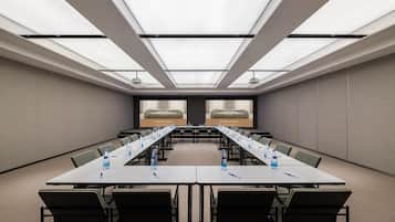 Un salón de conferencias con una larga mesa, sillas y una pantalla mostrando la marca del hotel.
