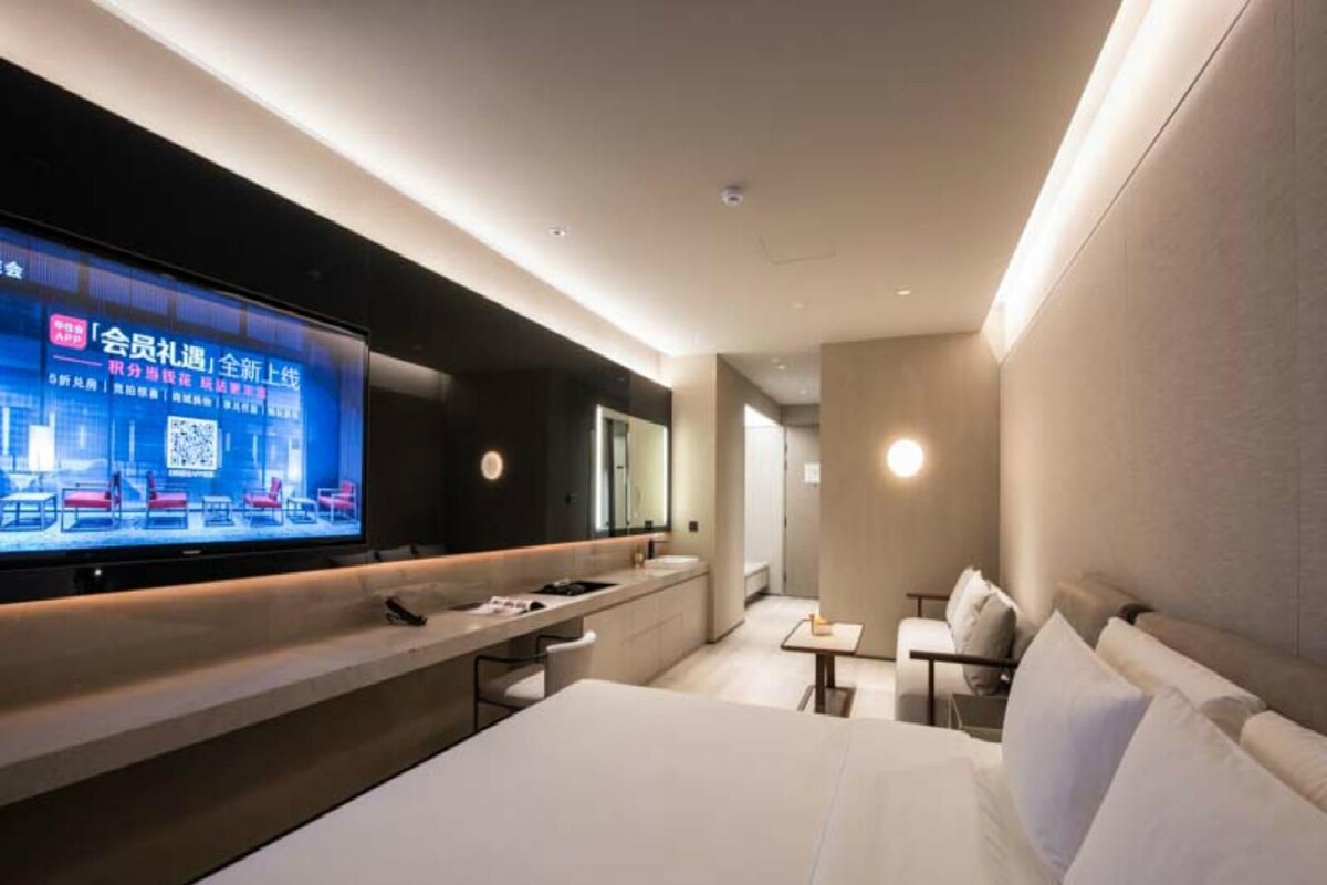 Une chambre d’hôtel moderne dotée d’un grand lit, d’un téléviseur à écran plat fixé au mur, d’une petite table et d’un coin salon avec un canapé.