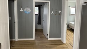Un couloir doté d’un plancher en bois, de murs gris et de moulures blanches. Les murs sont décorés de motifs maritimes, notamment des ancres et une enseigne sur laquelle on peut lire : « Ambiance plage uniquement ».