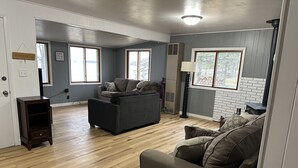 Un salon spacieux doté d’un parquet en bois, d’un canapé gris, d’un canapé marron et d’une petite table d’appoint en bois.