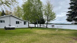 Une maison avec un grand réservoir d’eau dans la cour, un quai au bord du lac et une zone herbeuse avec des arbres.
