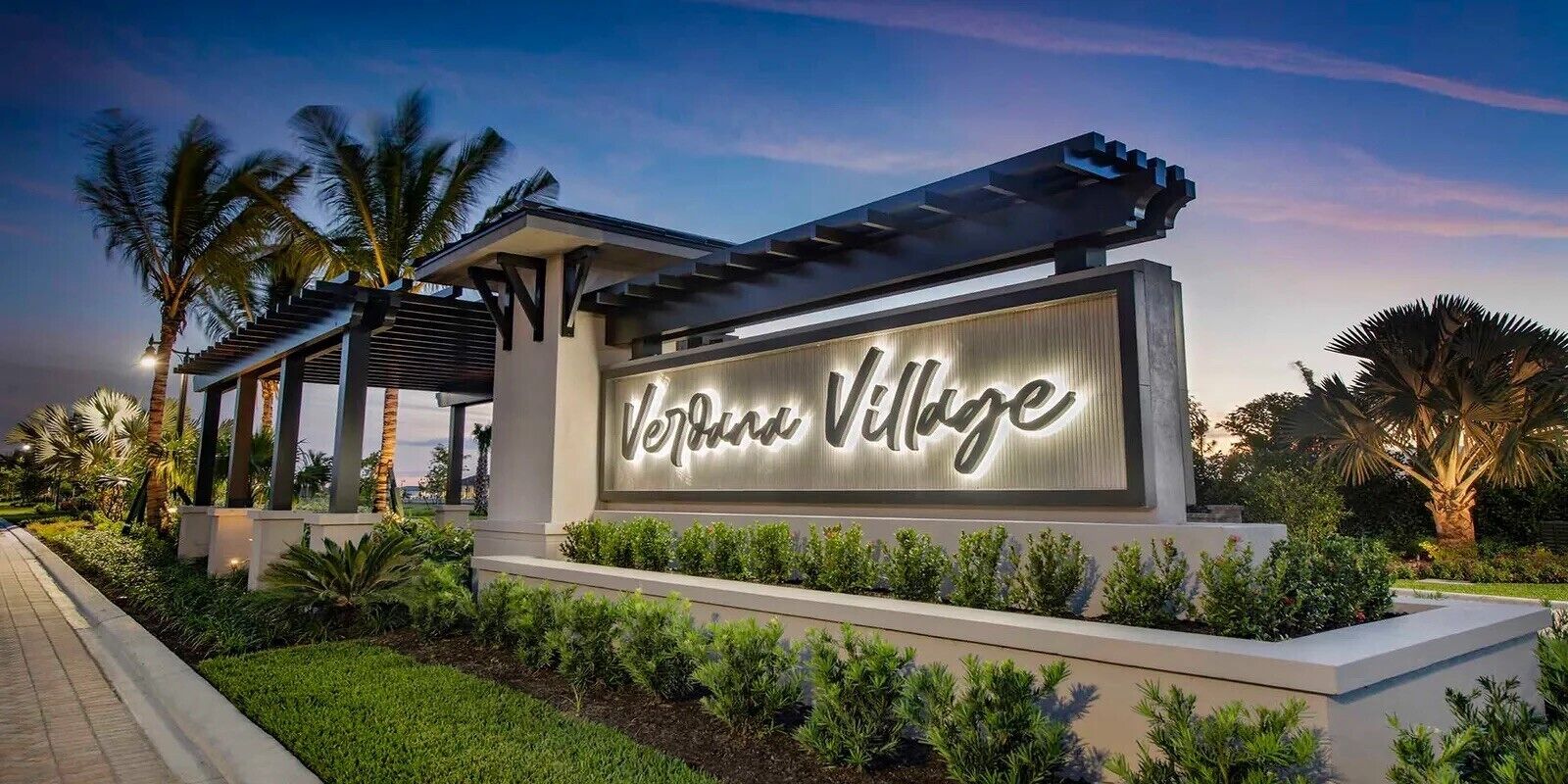 A sign for 'Verde Village' with a modern design, surrounded by well-maintained landscaping and palm trees.
