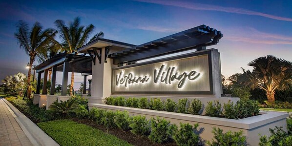 A sign for 'Verde Village' with a modern design, surrounded by well-maintained landscaping and palm trees.