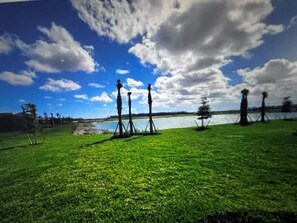 A grassy field with a body of water and trees in the background.