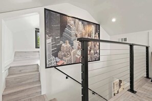 Un escalier orné d’une fresque représentant un paysage urbain, avec une rampe en métal noir et un intérieur blanc.