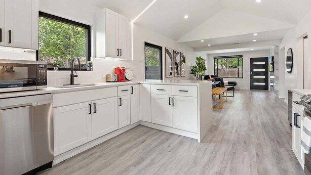 Una cucina moderna con mobili bianchi, un forno a microonde integrato e un'area pranzo con tavolo e sedie.