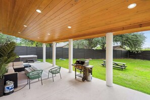 An outdoor patio with a wooden ceiling, a grill, a dining table, and a seating area. - Modern 5BR | 14 Guests | Hot Tub | Mins to DT SXSW (Austin)