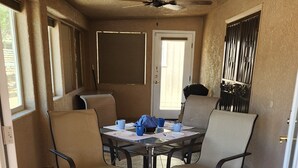 Zona pranzo con tavolo rotondo circondato da quattro sedie, una ventola a soffitto e una porta che dà all'esterno.