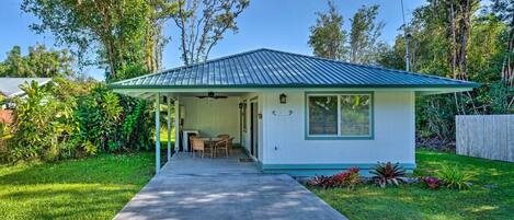 A small, single-story building with a green roof and white walls, featuring a covered porch with a table and chairs.