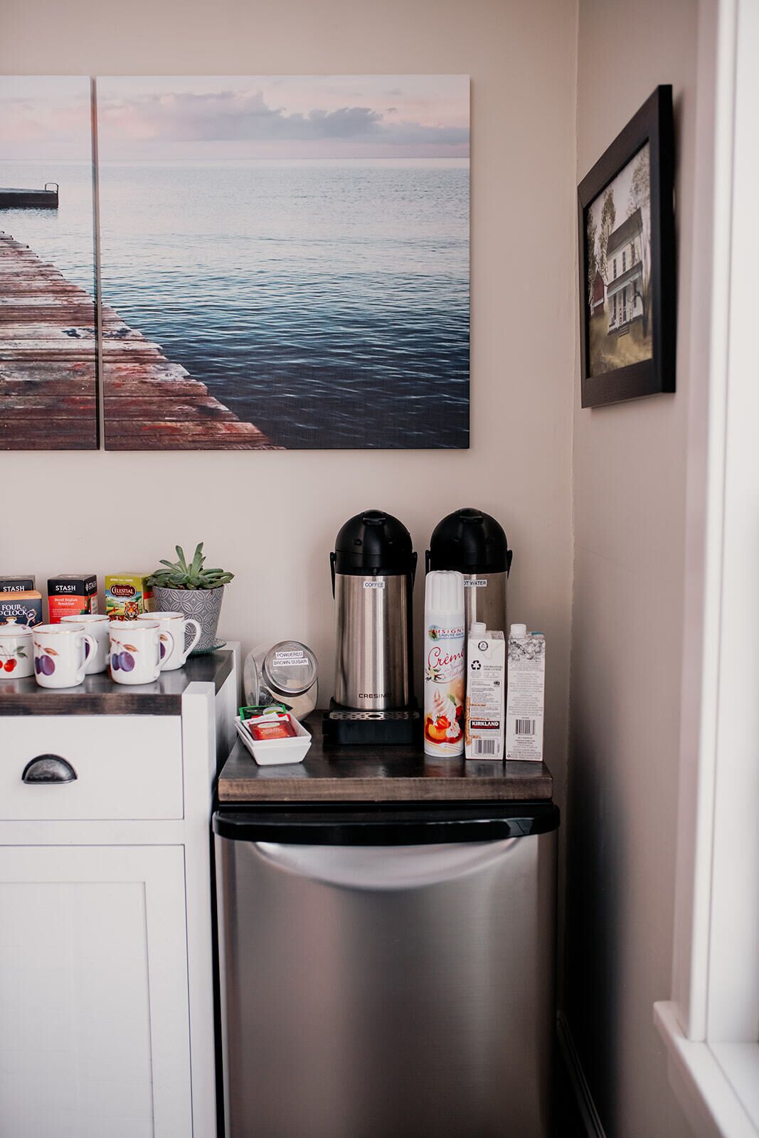 A kitchen with a stainless steel refrigerator, a coffee maker, and a water dispenser. There are mugs and a plant on the counter.