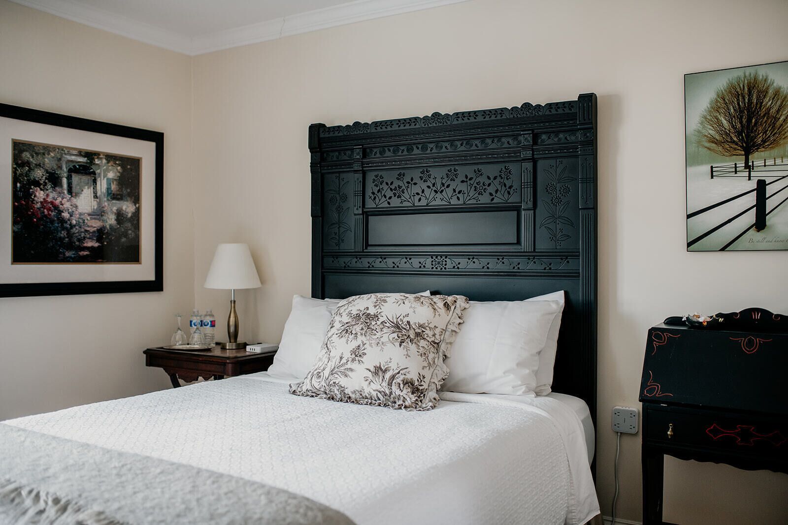 A neatly made bed with a floral pillow, a bedside lamp, and a framed picture on the wall.