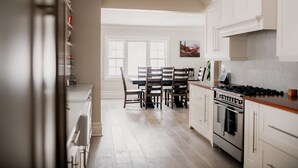 Een keuken met witte kastjes, een eettafel met stoelen en een groot raam.