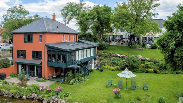 Een gebouw met twee verdiepingen, voorzien van een groen balkon, een vijver en een gazon met stoelen.